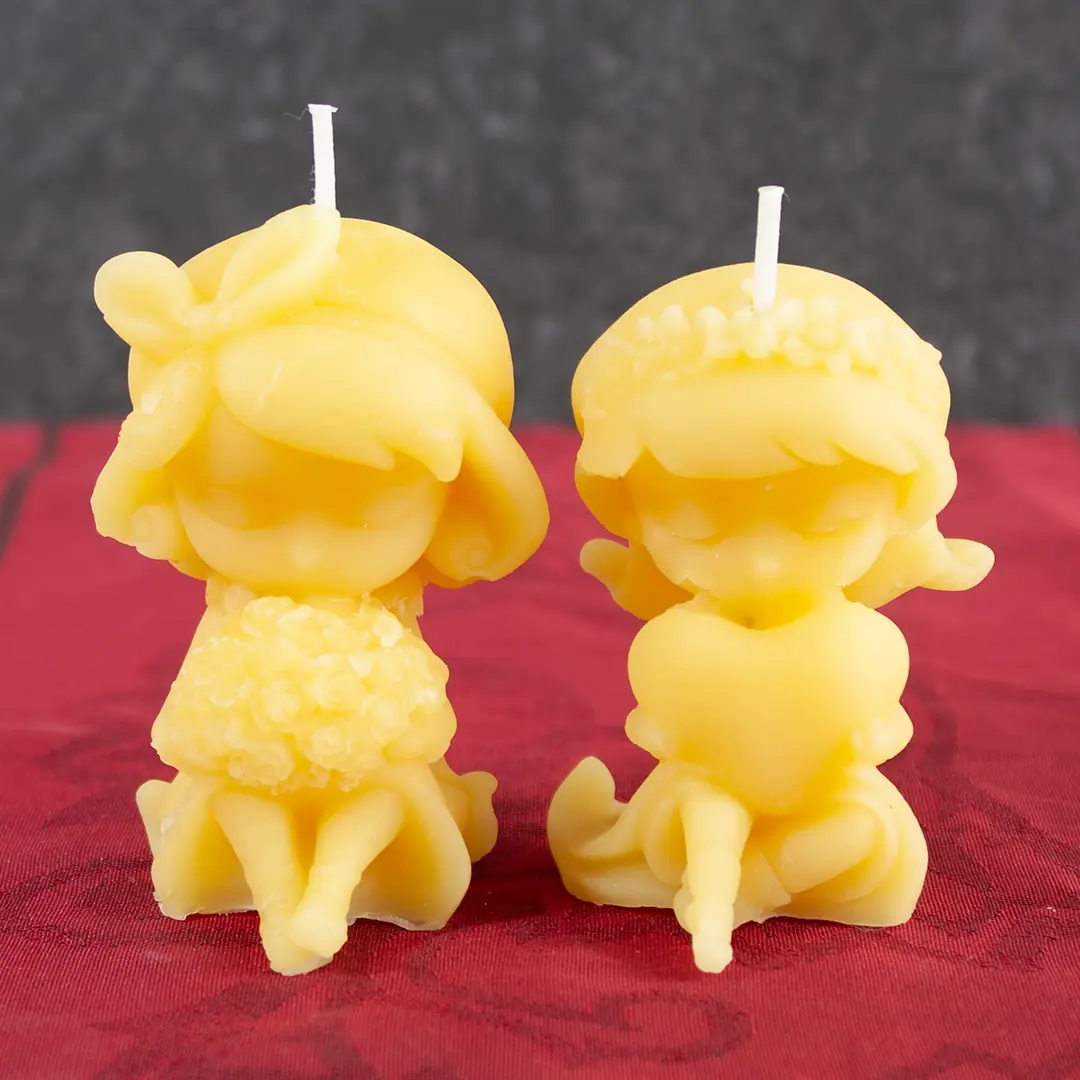 Goldgelbe Bienenwachs-Kerzen in Form von zwei sitzenden Mädchen mit Blumenstrauß und Herz
