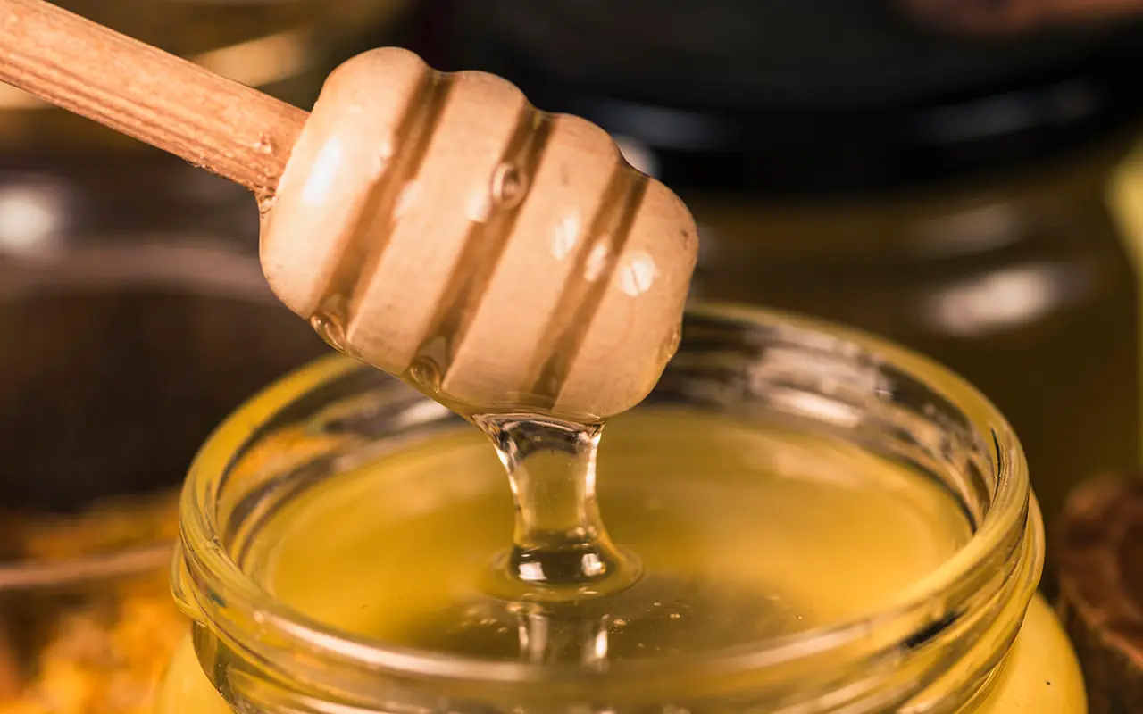 Goldener flüssiger Honig tropft von Holzlöffel zurück ins Glas - Imkerei Genzel Gera