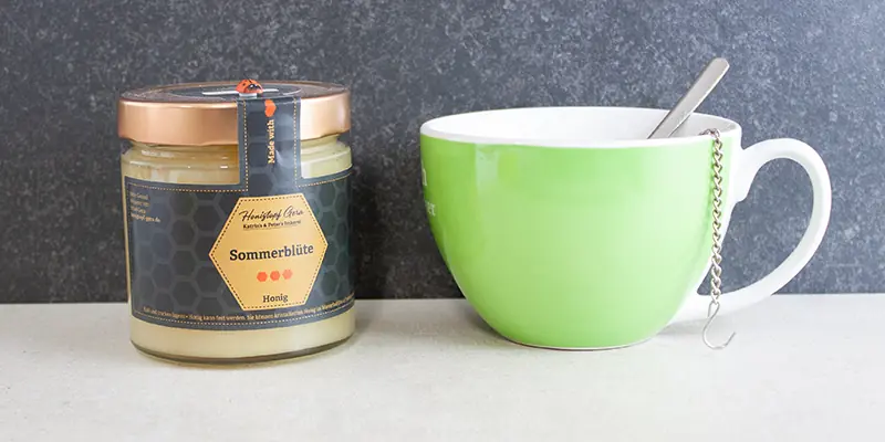 Honigglas neben Teetasse mit dampfendem Tee bei Erkältung im Winter