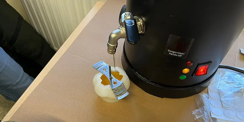 Imker gießt flüssiges Bienenwachs in Kerzenformen in einer Werkstatt