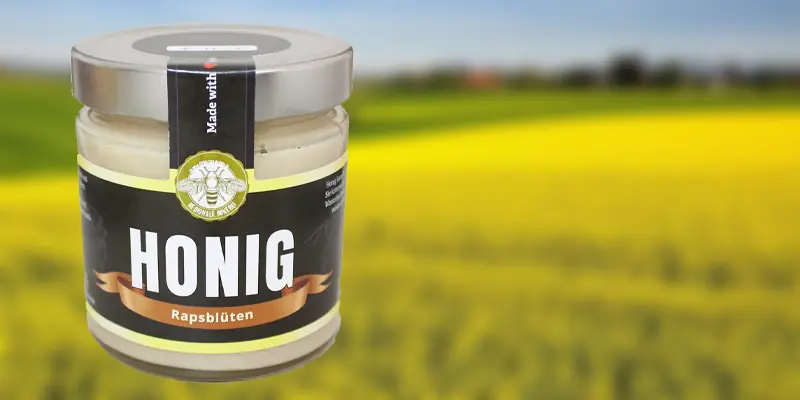Cremiger Rapshonig aus Gera vor blühendem Rapsfeld Rapshonig - Glas mit cremigem hellgelbem Rapshonig vom Imker vor gelbem Rapsfeld in Thüringen